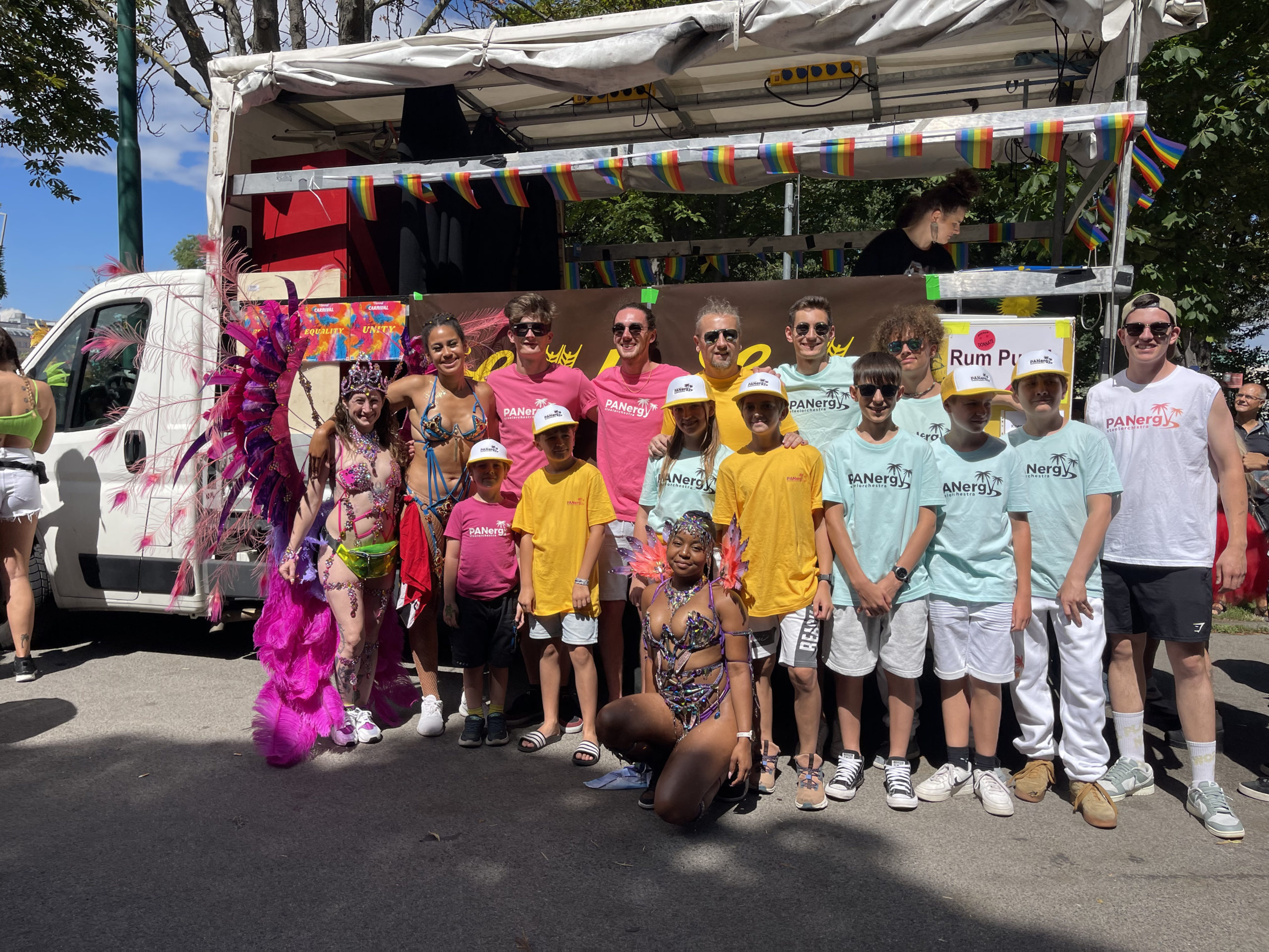 Kinder und Jugendliche sind bei unserem Carnival herzlich willkommen, und wir sorgen stets für ein abwechslungsreiches Kinderprogramm am Tag des Carnivals. Auf dem Foto sieht man neben den Obfrauen des Vereins (links) auch Panergy, die wir 2023 zum ersten Mal in Wien begrüßen durften. Panergy ist ein 16-köpfiges Steelpan-Orchester aus Tirol mit Mitgliedern im Alter von 10 bis 18 Jahren. Ihr Live-Konzert ist bis heute unvergessen und bleibt den Teilnehmerinnen und Teilnehmern des Carnivals in bester Erinnerung.