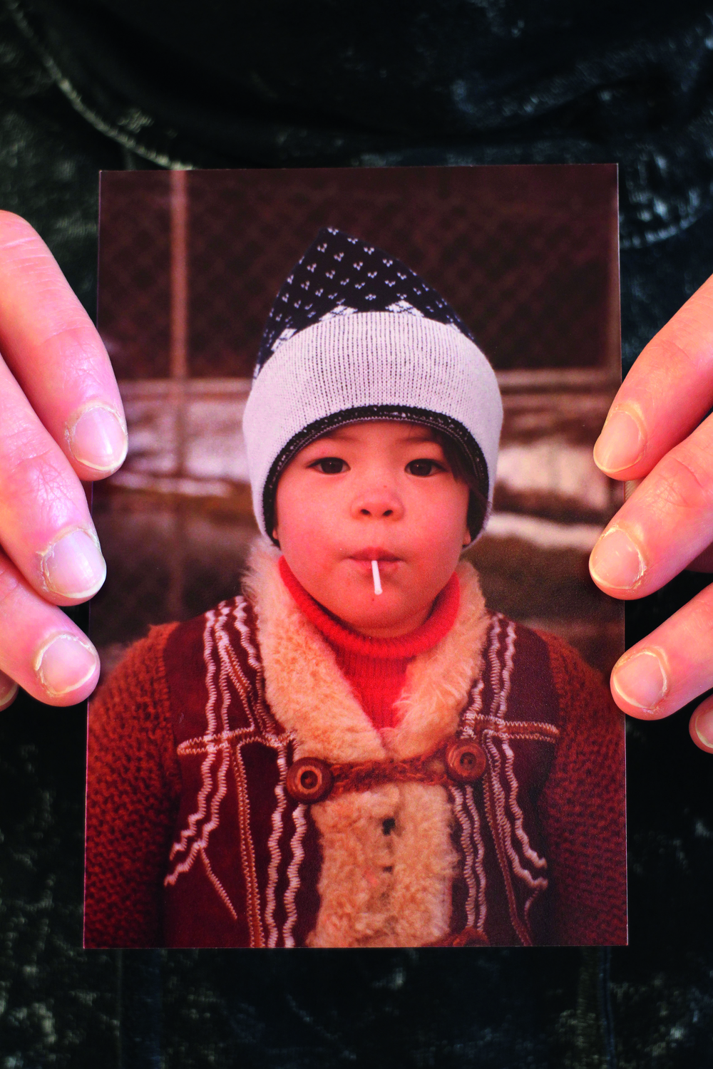 Man sieht ein Kinderfoto, das von beiden Seiten gehalten wird, wobei man nur  die Finge der haltenden Person sieht