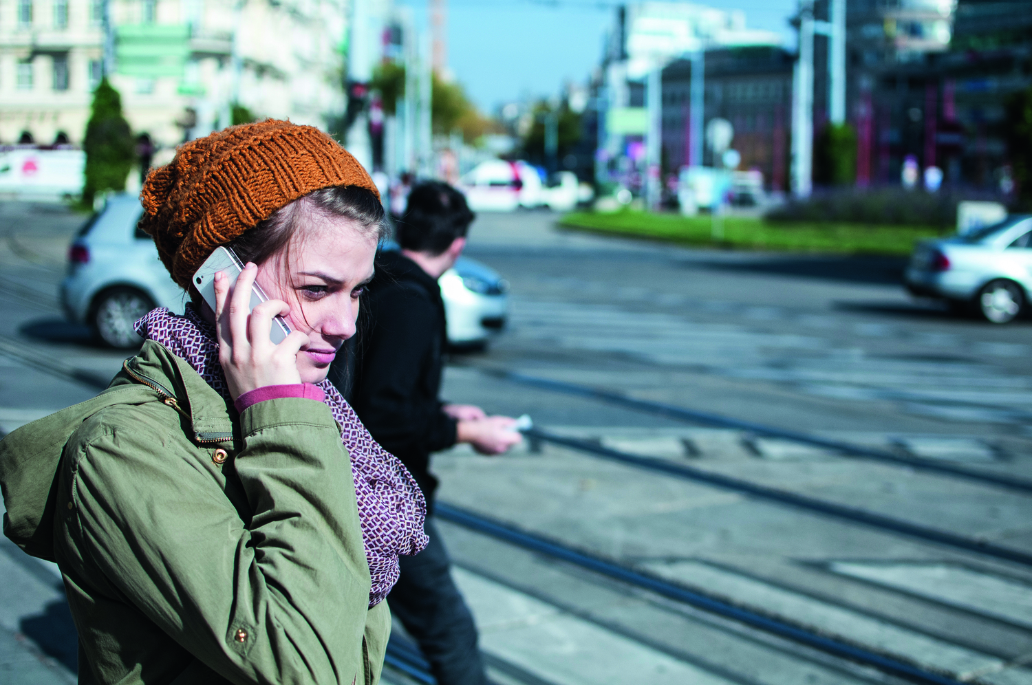 Sujet-/Szenenfoto, auf einer Straße steht eine junge Frau in Winterkleidung und hält ein Handy an ihr Ohr