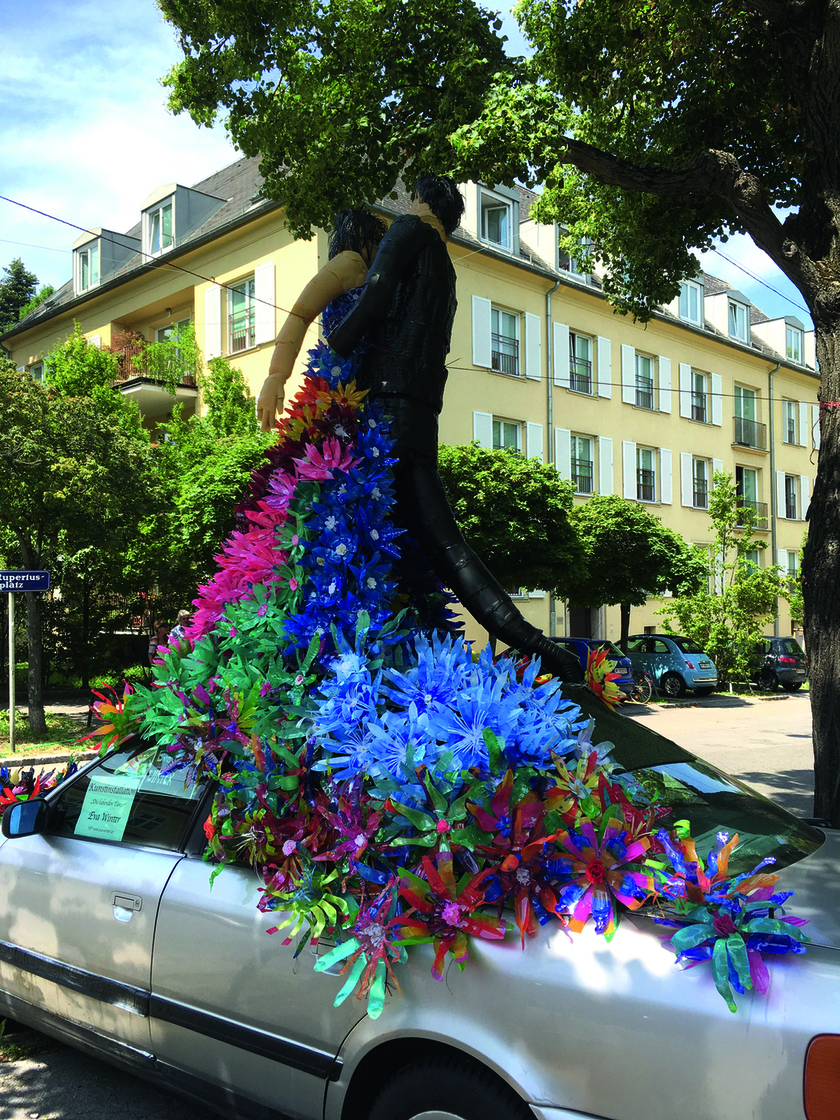 Auf einem silbergrauen Auto steht eine Blumenwiese mit einem Liebespaar aus PET-Flaschen