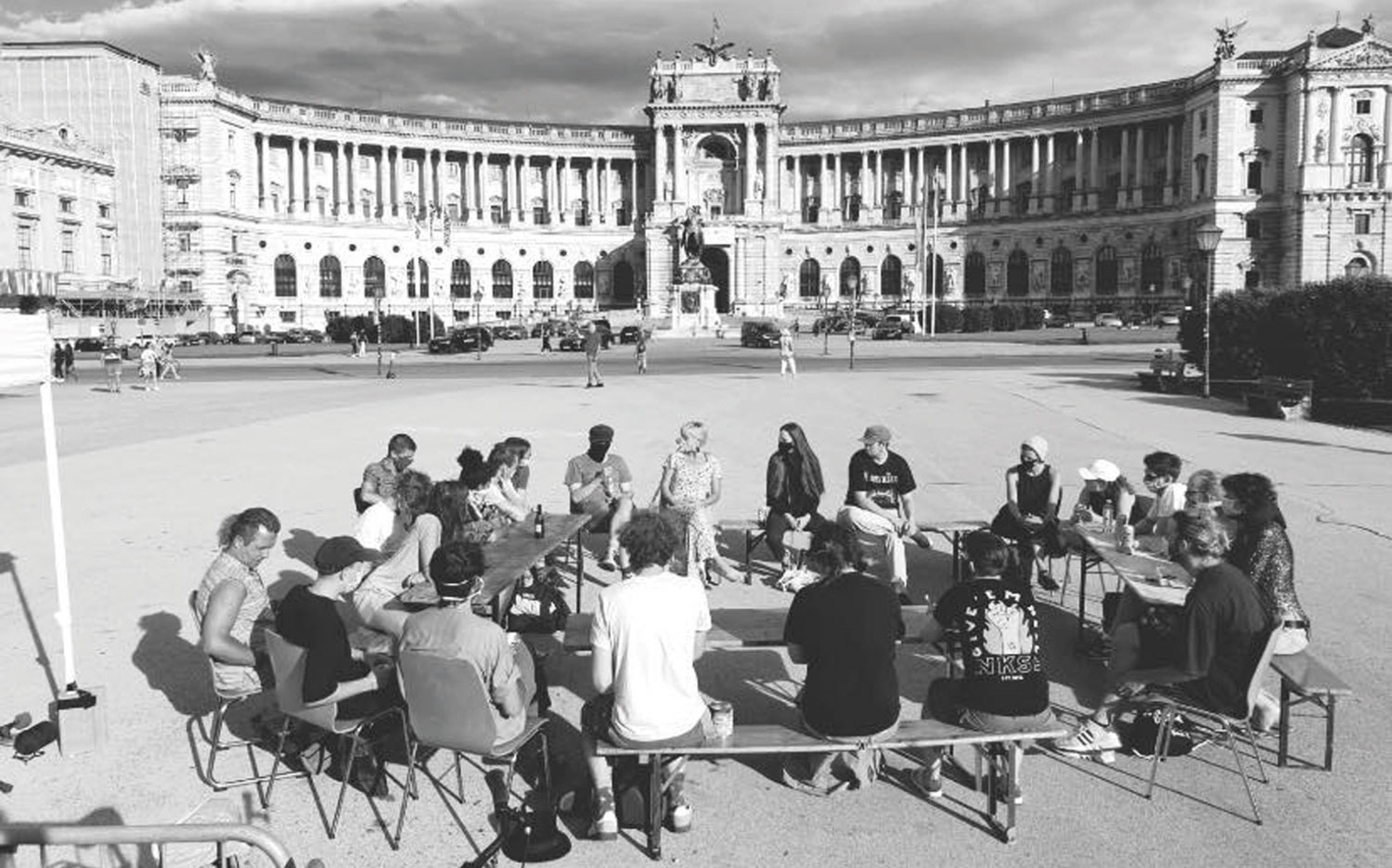 Schwarzweißbild, Wiener Heldenplatz, auf dem auf Bänken im Kreisformat eine Gruppe Menschen sitzen