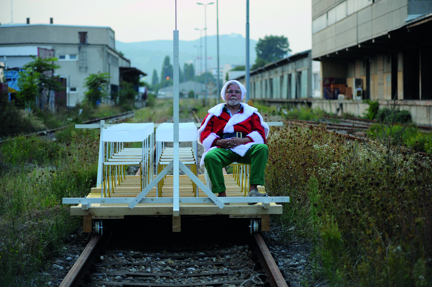 Ehemaliges Bahnhofsgelände, eine stillgelegte Schiene, auf der ein alter, offener Wagen steht, darin sitzt ein Mann mit grüner Hose und rot-weißer "Weihnachtsmann"-Jacke