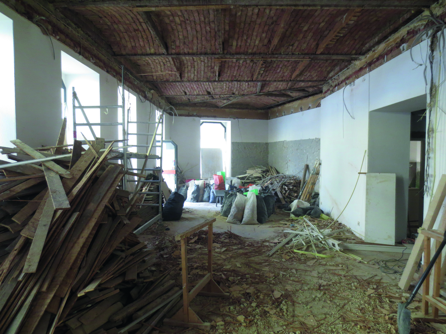 Man sieht einen der Räume der Bibliothek im Umbau, der Boden ist aufgerissen, die Holzlatten liegen herum, die Decke aus Holz ist freigelegt, die Wände sind regallos ...