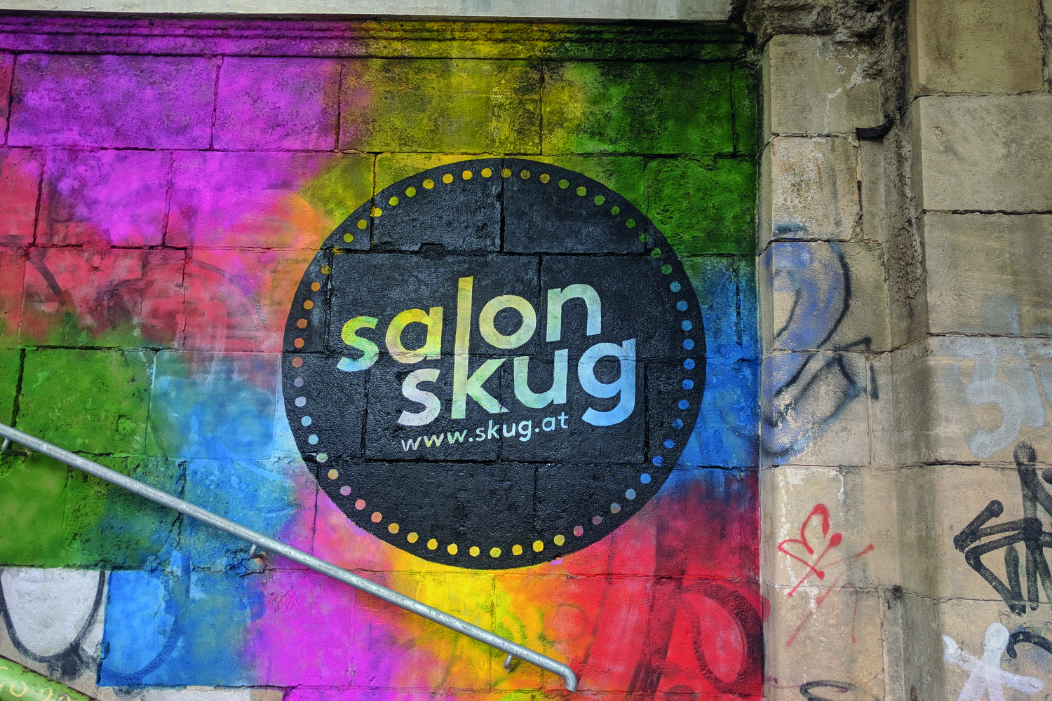 Eine bunt-flächige Graffiti-Wand, auf der das Logo des "Salon skug" platziert ist