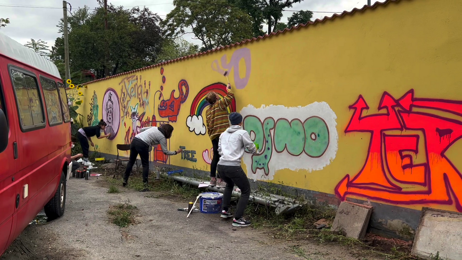 Graffiti-Künstler:innen arbeiten an einer gelben Wand im öffentlichen Raum.