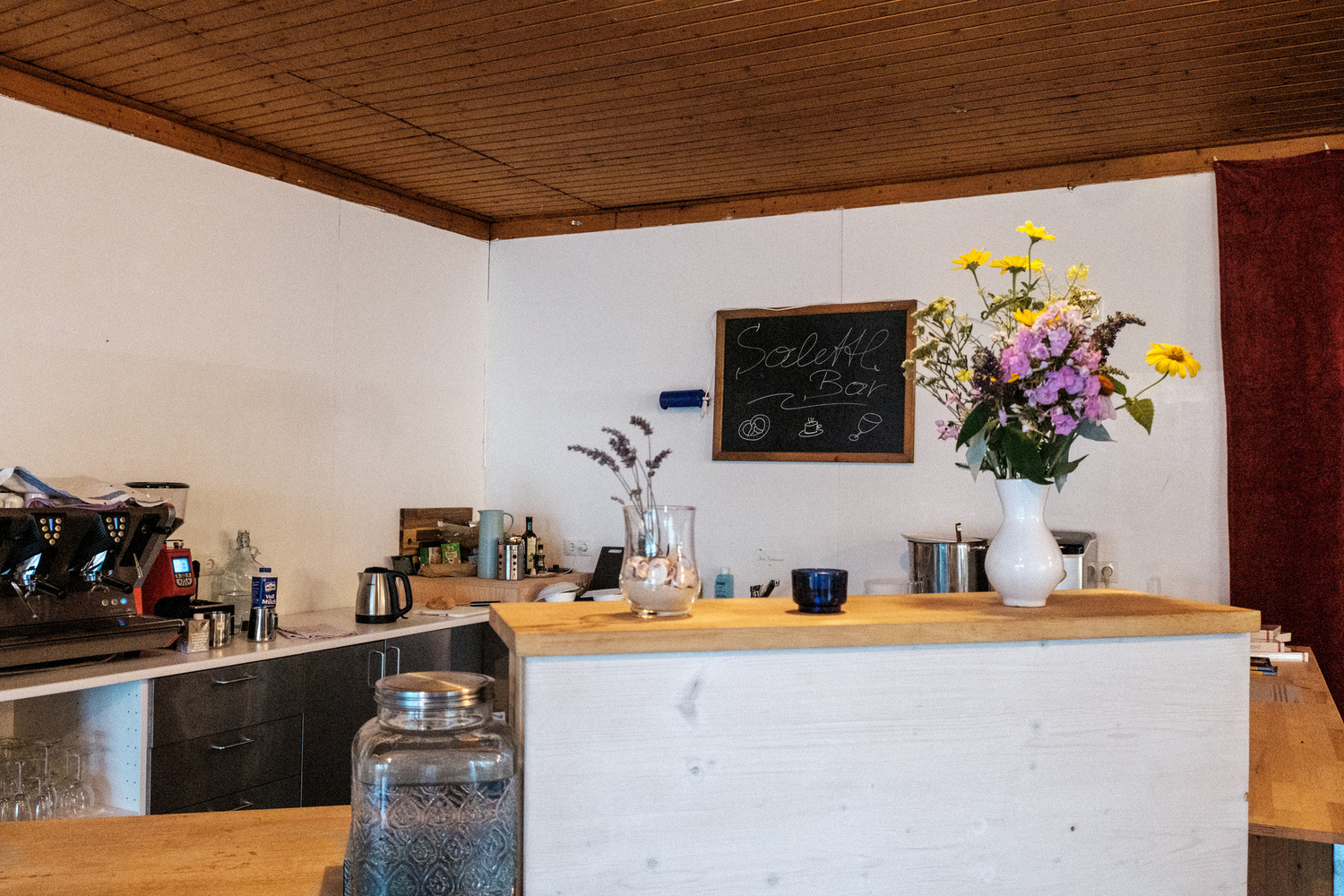 Das Foto zeigt eine Art Gemeinschaftsküche mit einer Bar, auf der ein bunter Wiesenblumenstrauß steht.