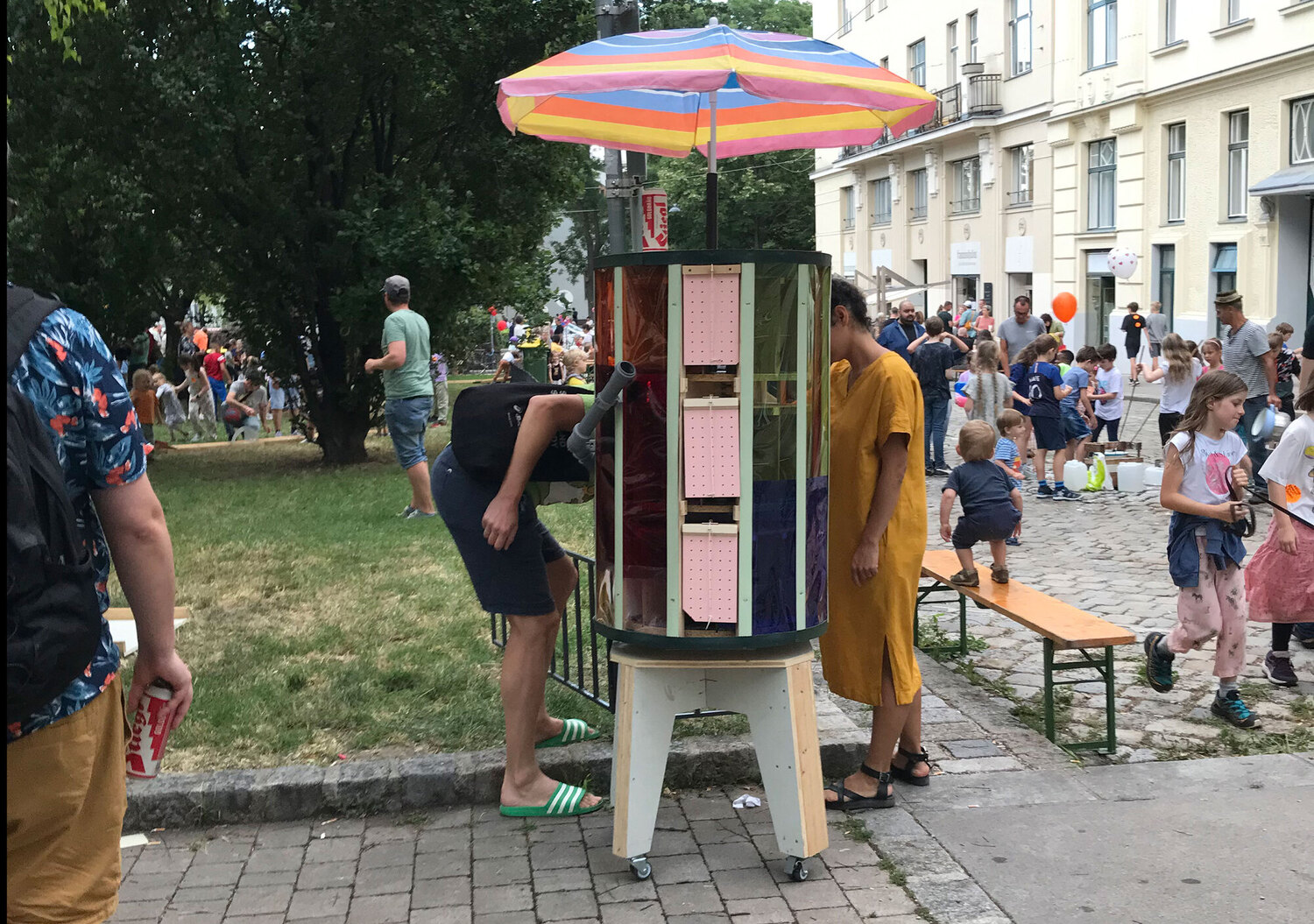 The Auto-mate steht im öffentlichen Raum, mehrere Personen untersuchen das von einem bunten Regenschirm überdache Objekt.