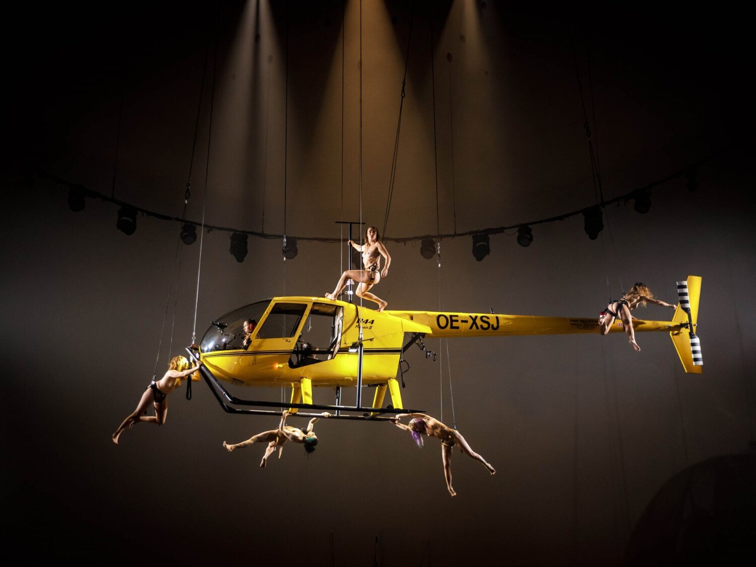 Szenenfoto aus dem Stück, man sieht nackte Performer:innen auf einem gelben Hubschrauber.