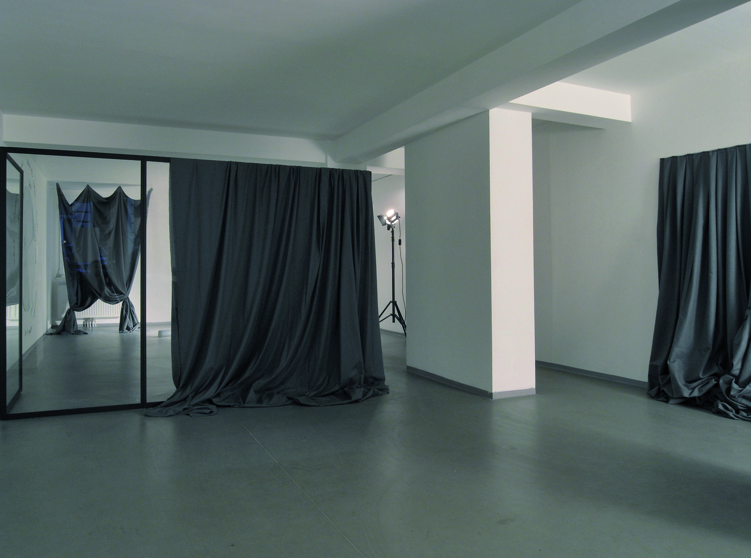  Jenni Tischer: "Alle eure Farben", 2009, Ausstellungsansicht Saprophyt: ein weißer Ausstellungsraum, in dem eine Rauminstallation aus grauen Stoffen, Gerüst, Spiegel und einem Lichtspot zu sehen ist