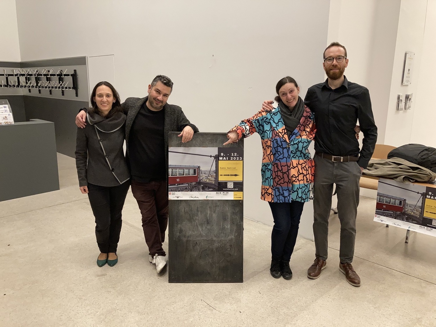 Das Team des Festivals in einem Foyer, in der Mitte eine graue Säule mit dem Plakat zum Festival.