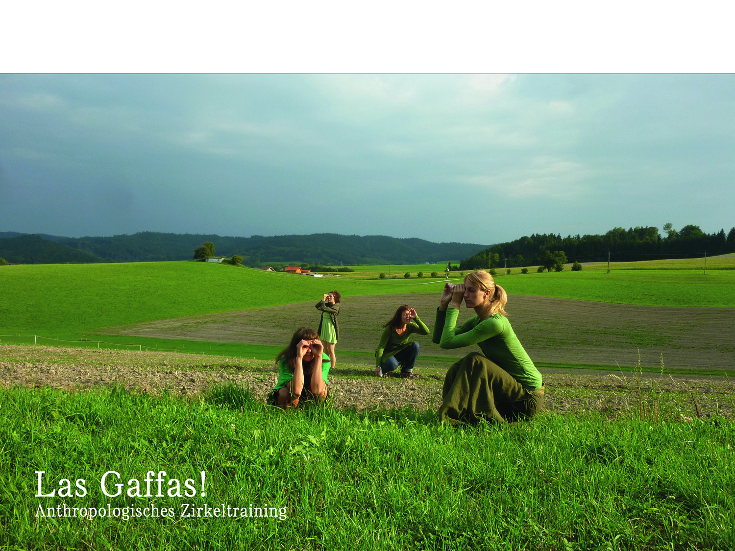 4 Frauen knien und stehen auf einem Feld, halten die Finger zu einem Fernrohr geformt und blicken in unterschiedliche Richtungen in der Landschaft