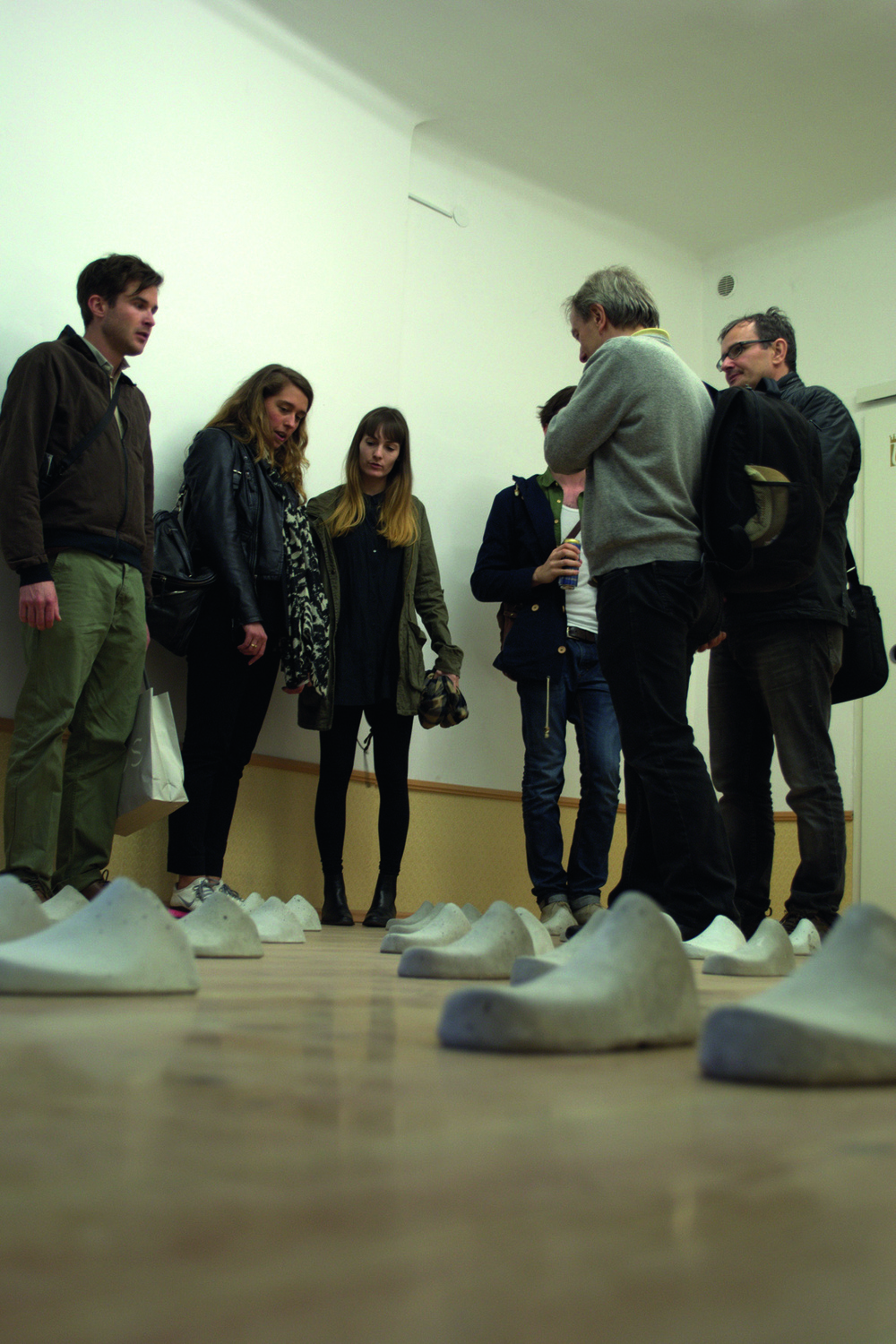 Mehrere Personen stehen in einem Ausstellungsraum, auf dessen Boden mehrere Schuhe aus Stein stehen