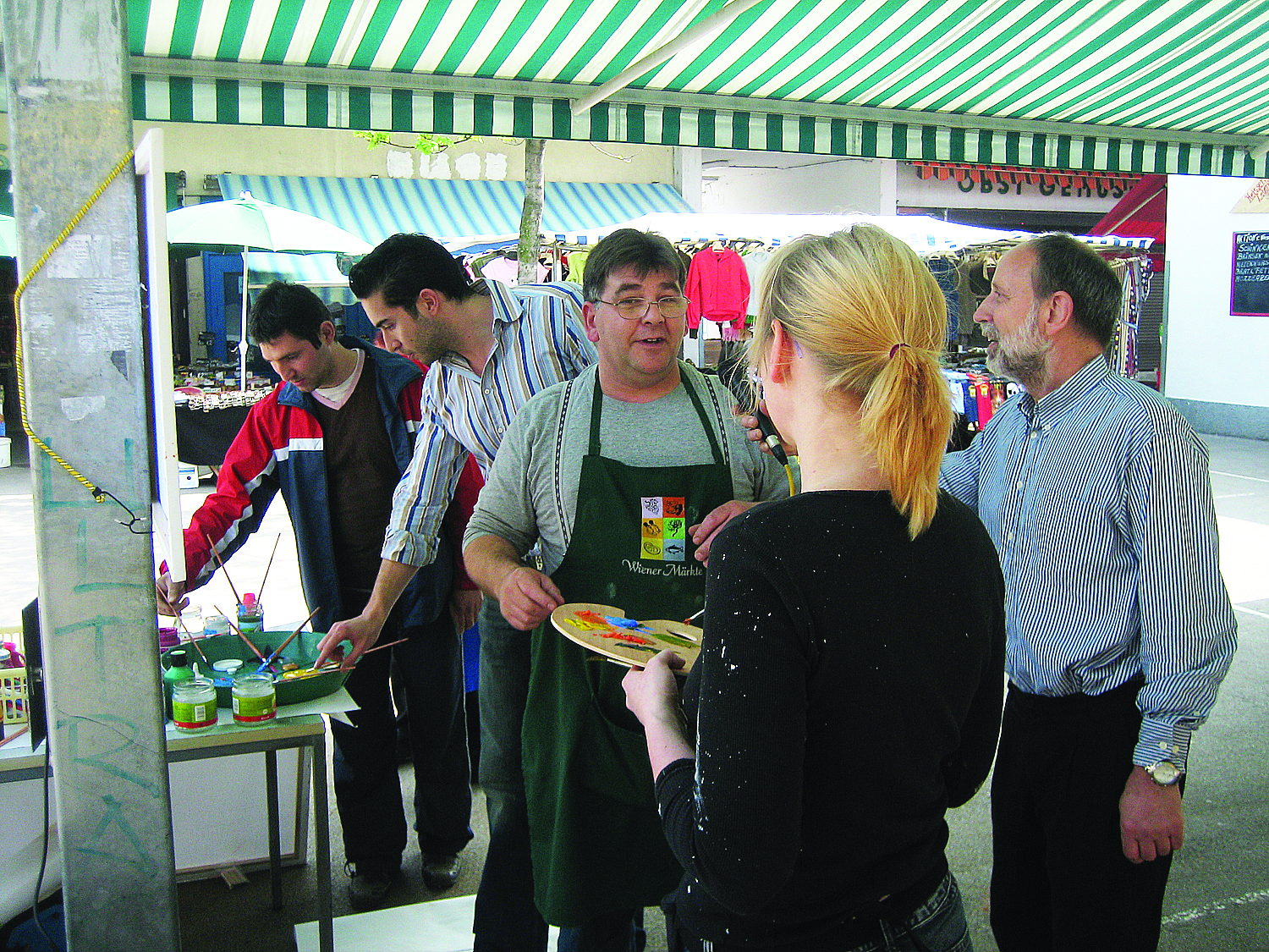 Menschen stehen auf einer Art Markstand und malen und plaudern