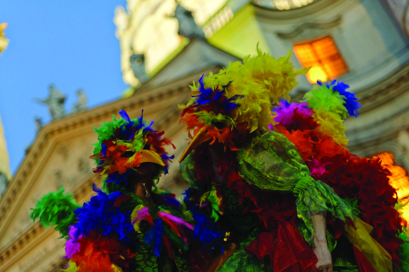 Personen in bunten Vogelkostümen und -masken vor der Wiener Karlskirche (Froschperspektive)