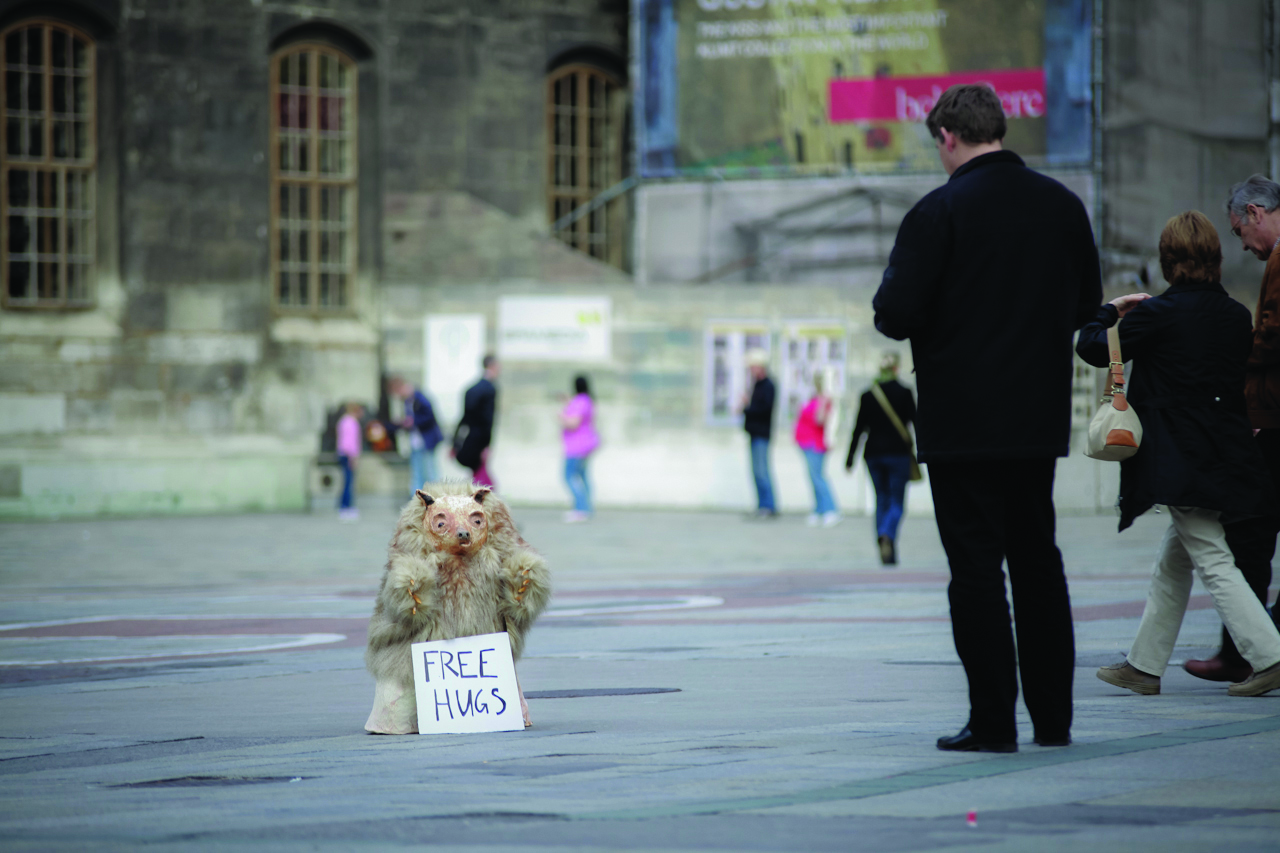 Ein kleines Faultier steht vor dem Stephansdom mit dem Schild "Free hugs" (Gratis-Umarmungen)