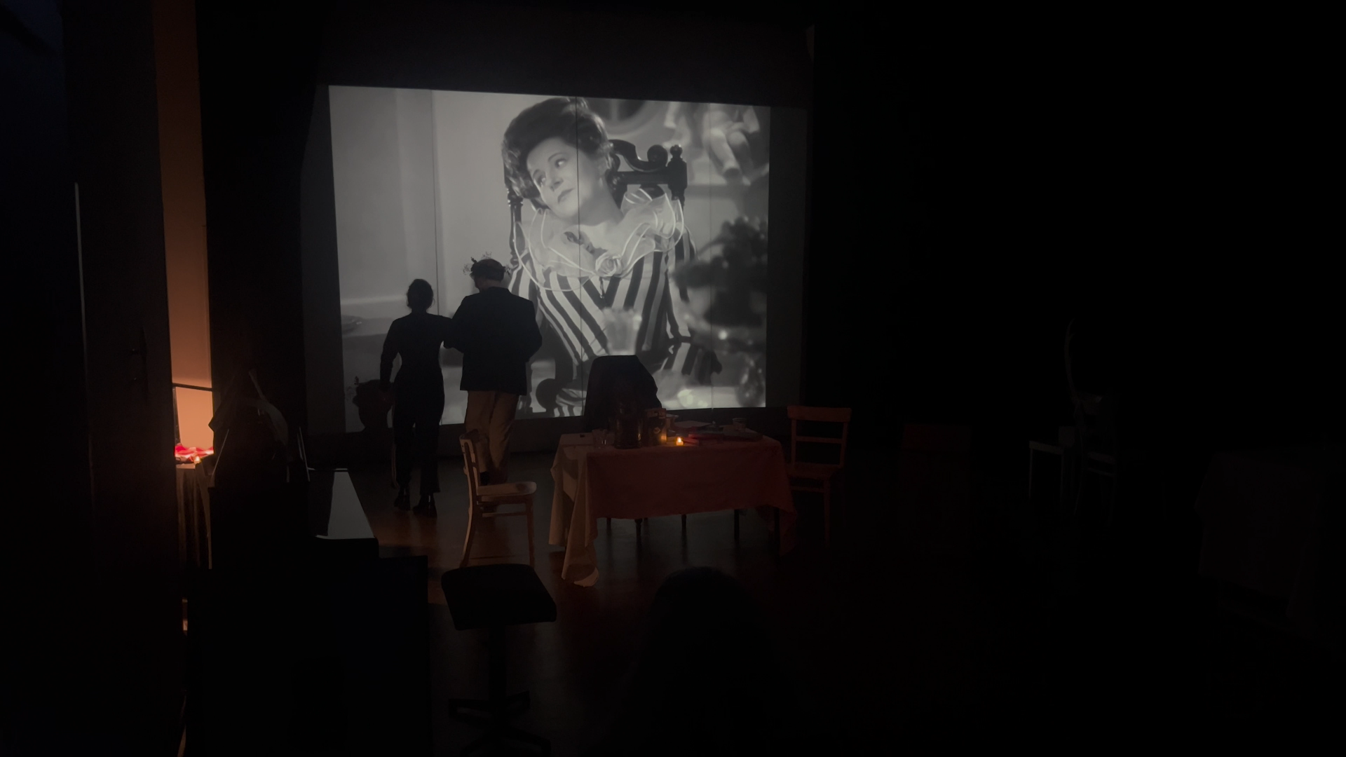 Die Leseprobe zu Jelineks Burgtheater wird vom Geist von Paula Wessely - live aus der Hölle – unterbrochen und in Der Engel mit der Posaune (den bekannten Selbstentnazifizierungsfilm) verwandelt. Dunkle Bühne mir großer Projektion von Wessely, davor Milo Rau und Mavie Hörbiger als Schattenumrisse beim Abendspaziergang.